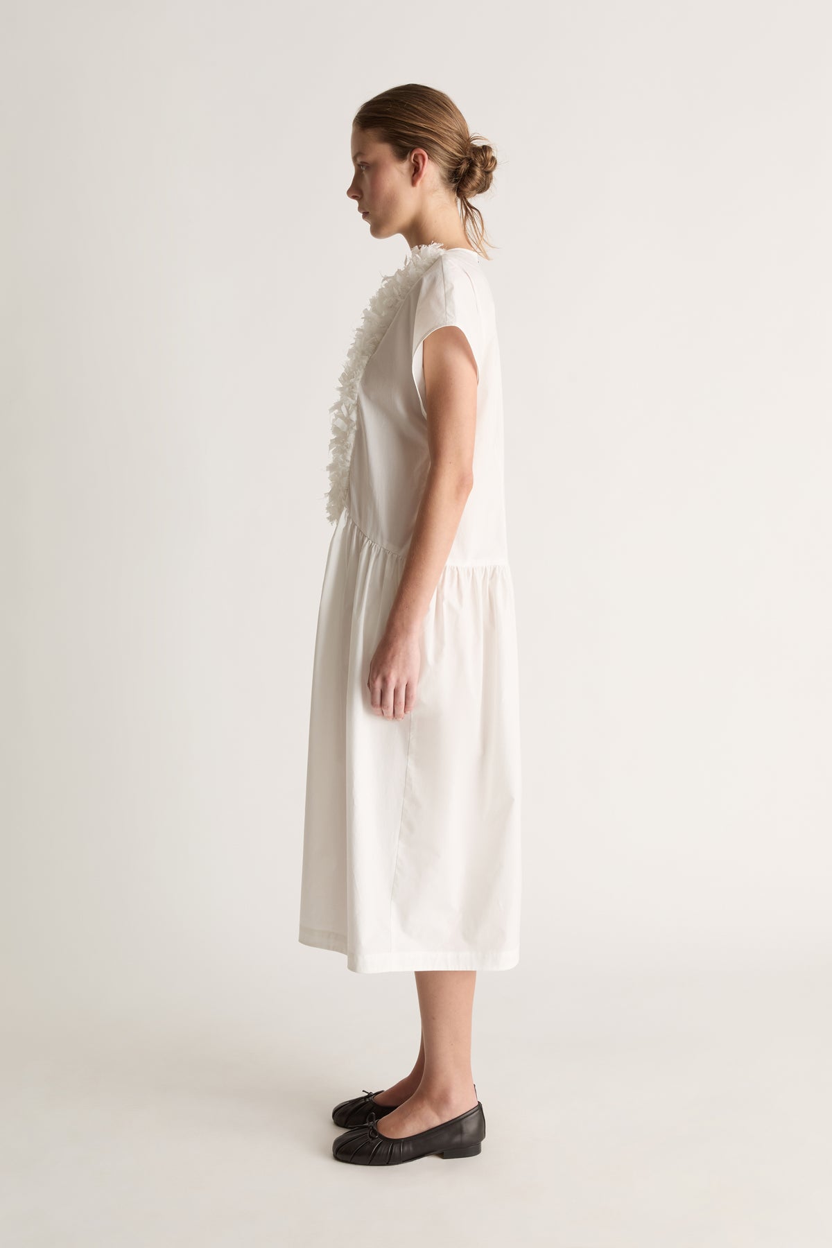 Side view of a white midi dress with cap sleeves, a ruffled front and gathered skirt.