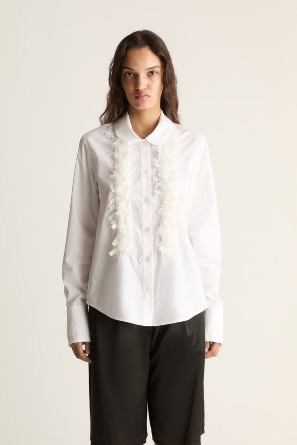 Close-up of a white shirt with round collar, ruffle ribbon down the front and long cuffs