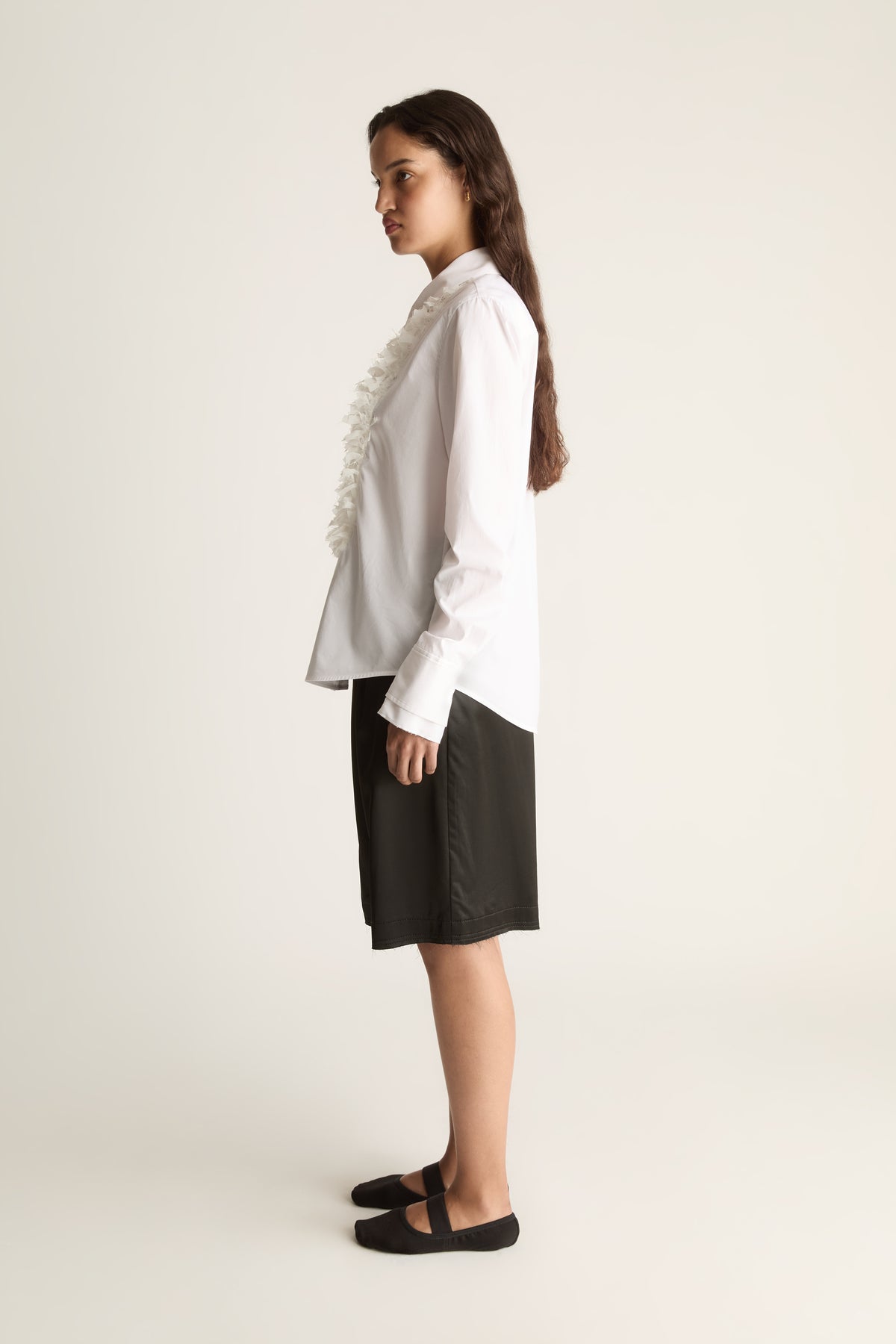 Side view of a woman glancing back in a white button-up shirt with ruffle trim and black shorts