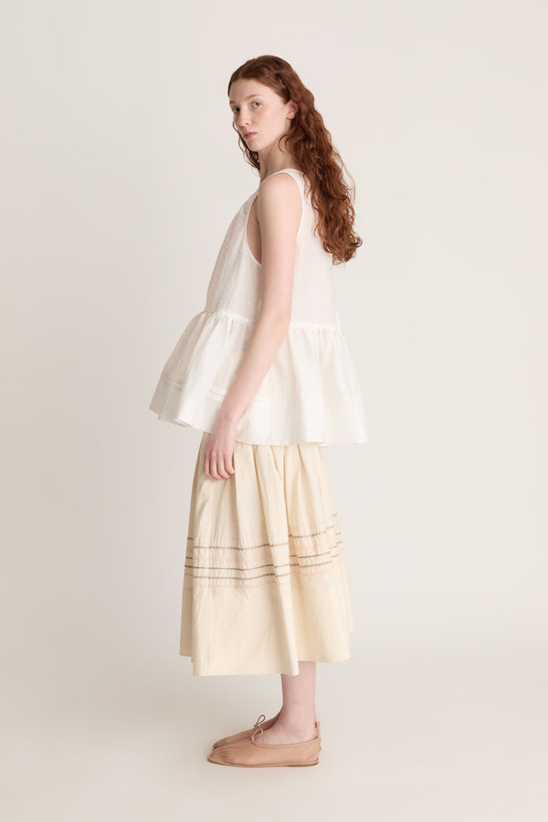 A woman wearing a white top with a peplum with a beige skirt on a white background