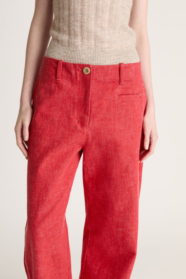 Woman wearing a beige knit cami top and red pants on a white background