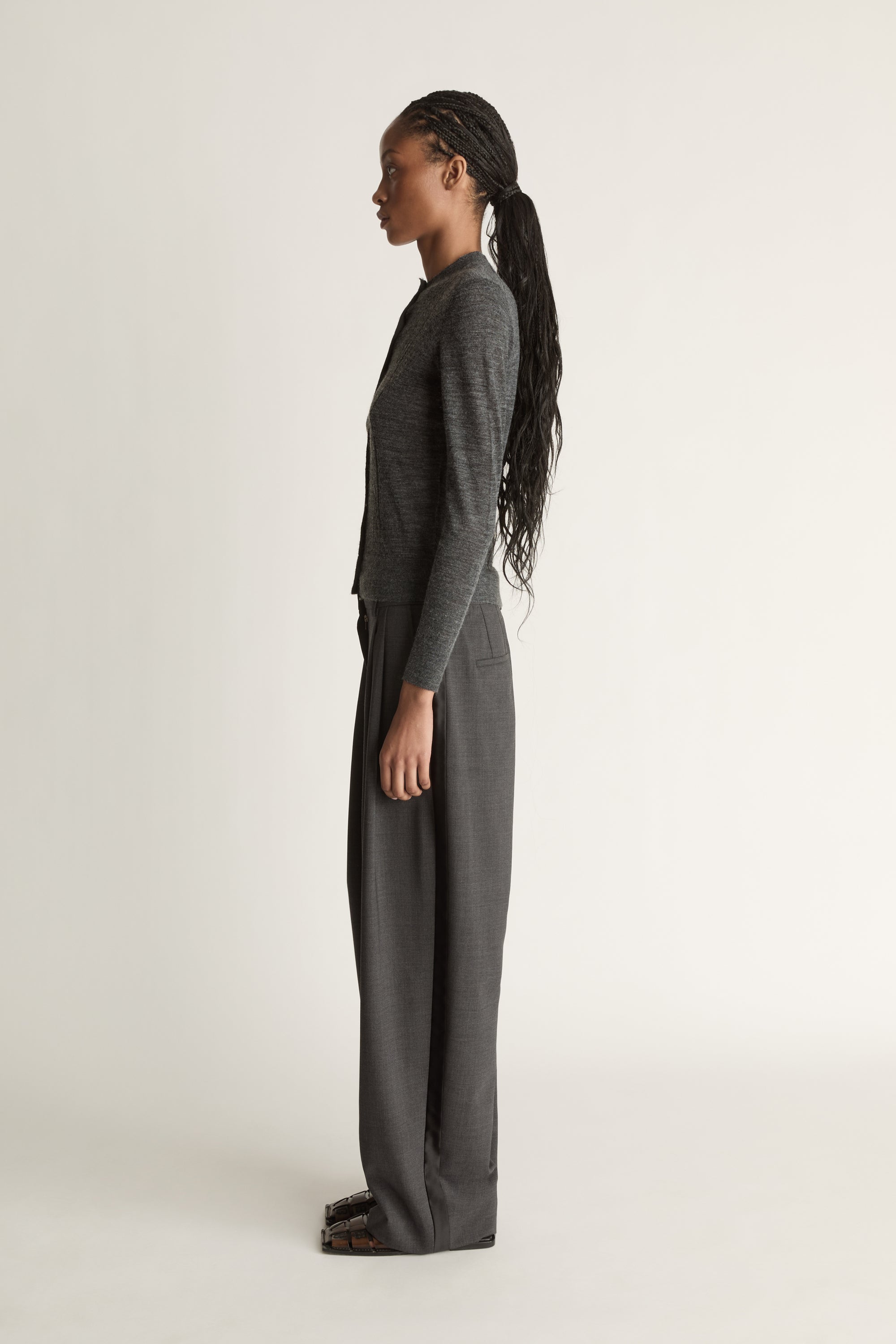 Woman wearing a grey cardigan and grey trousers on a white background