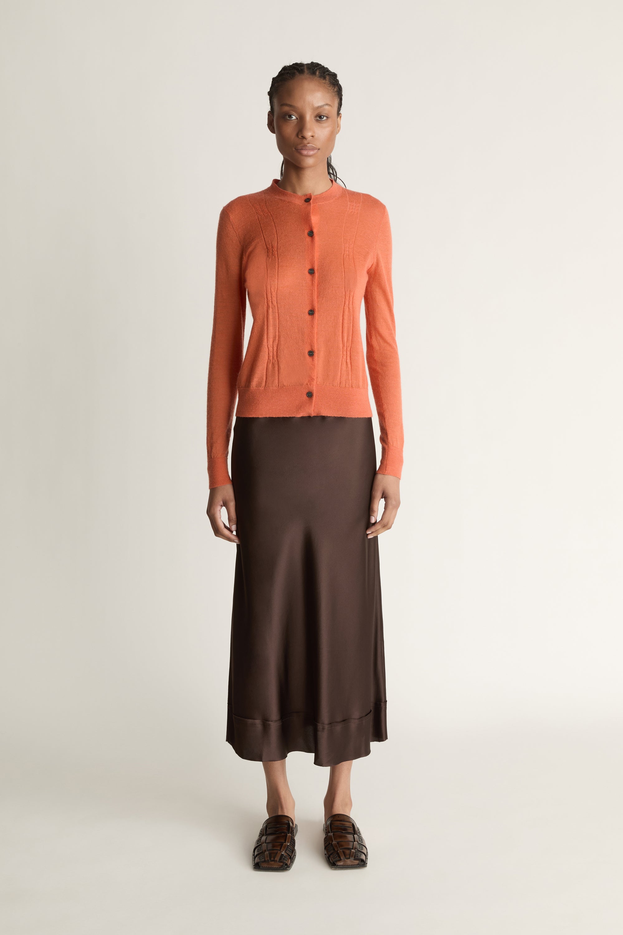 Woman wearing an orange cardigan and brown skirt on a white background