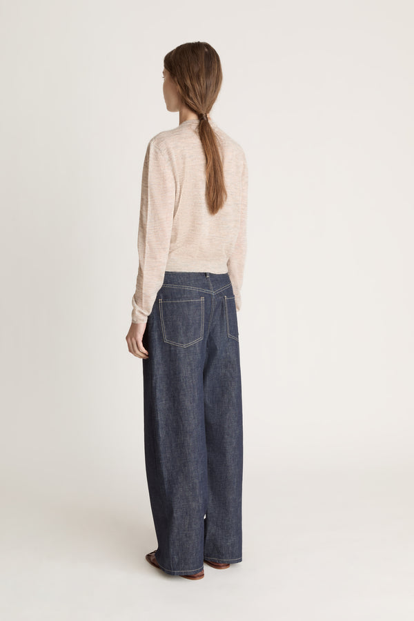 Person wearing a beige cardigan and dark jeans on a white background