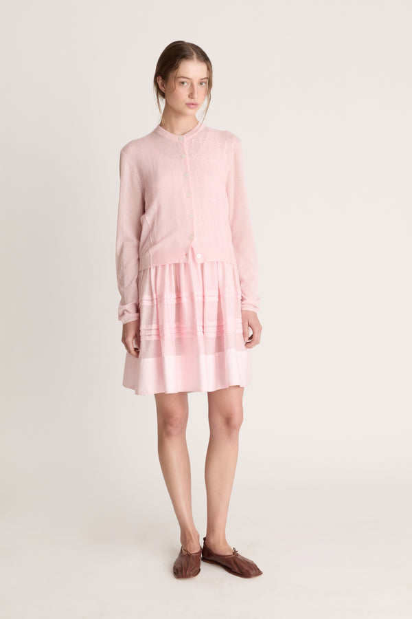 Woman wearing a light pink dress with a light pink knit cardigan on a white background