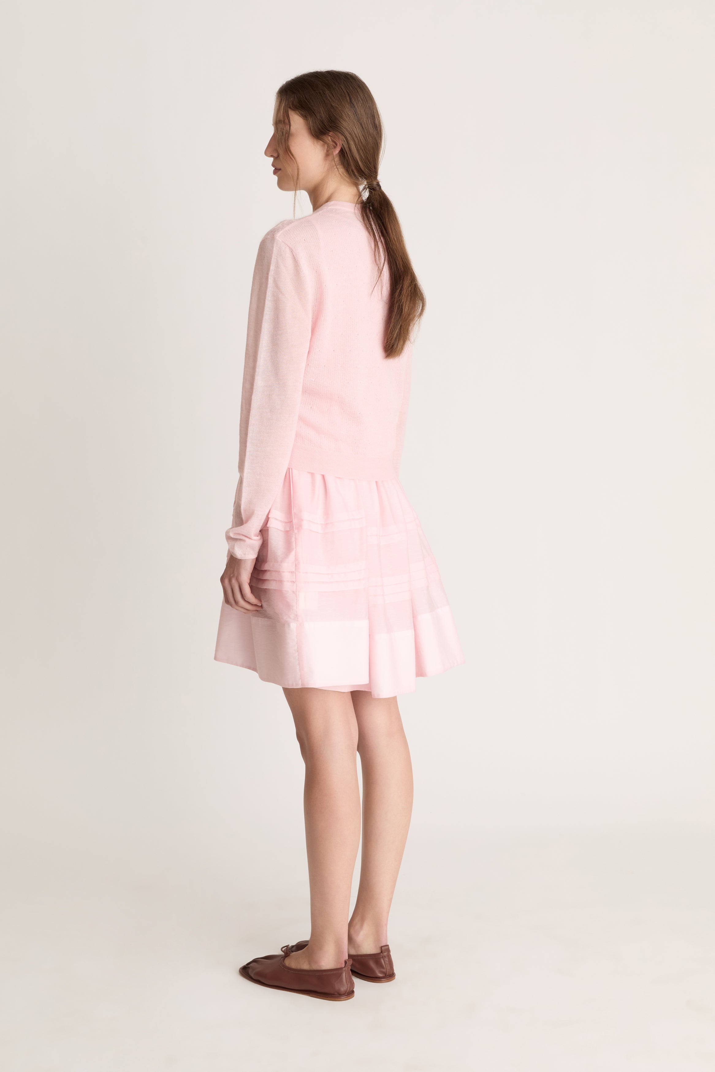 Woman wearing a light pink dress with a light pink knit cardigan on a white background