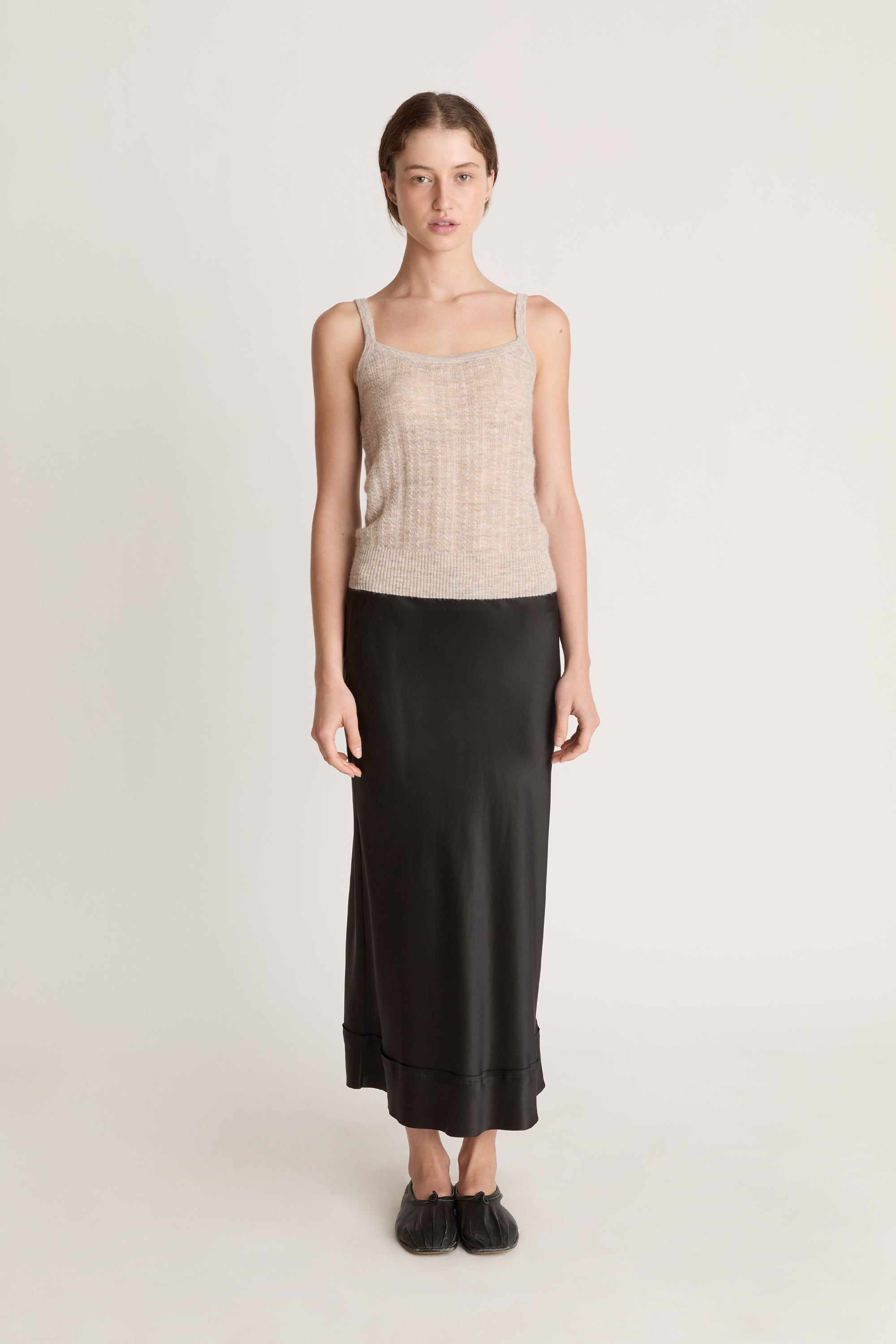Woman wearing a beige knit cami top and black skirt on a white background