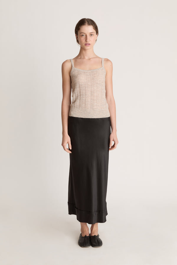Woman wearing a beige knit cami top and black skirt on a white background