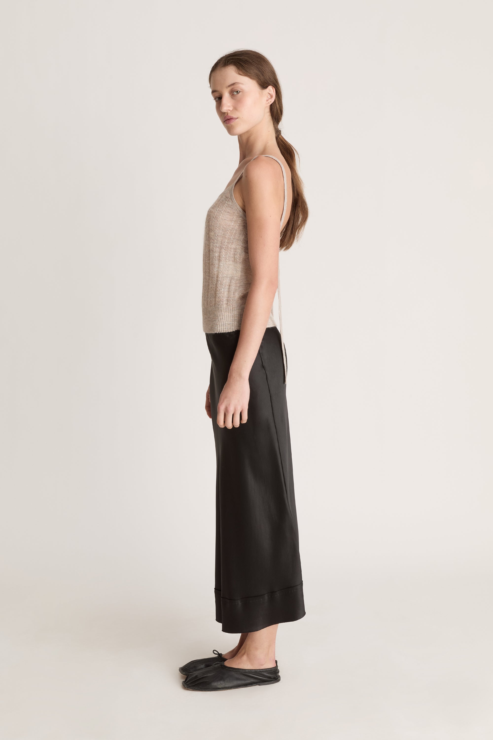 Woman wearing a beige knit cami top and black skirt on a white background
