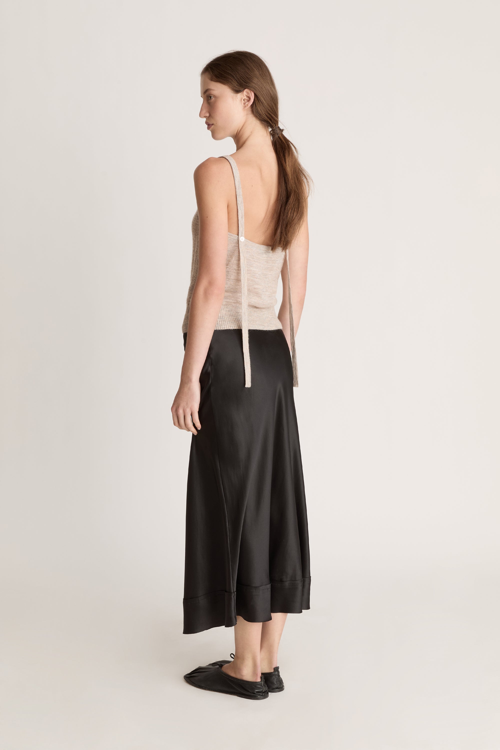 Woman wearing a beige knit cami top and black skirt on a white background