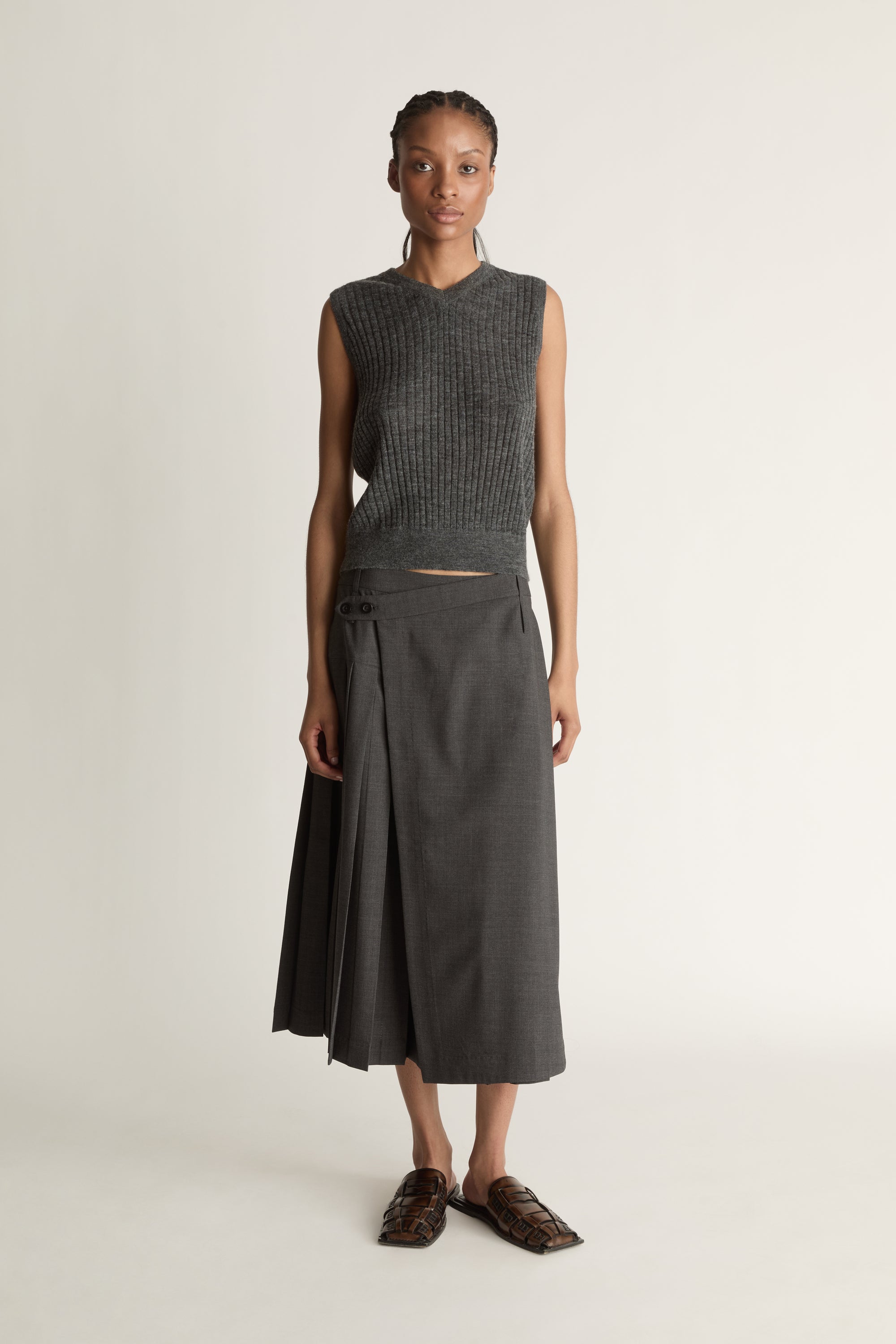 Woman wearing a dark gray sleeveless v neck knit top and skirt on a white background