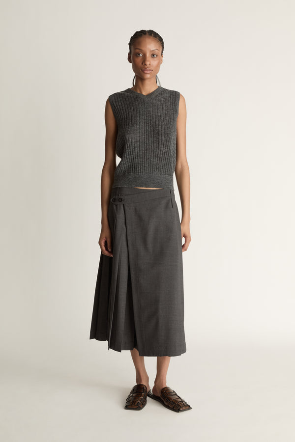 Woman wearing a dark gray sleeveless v neck knit top and skirt on a white background