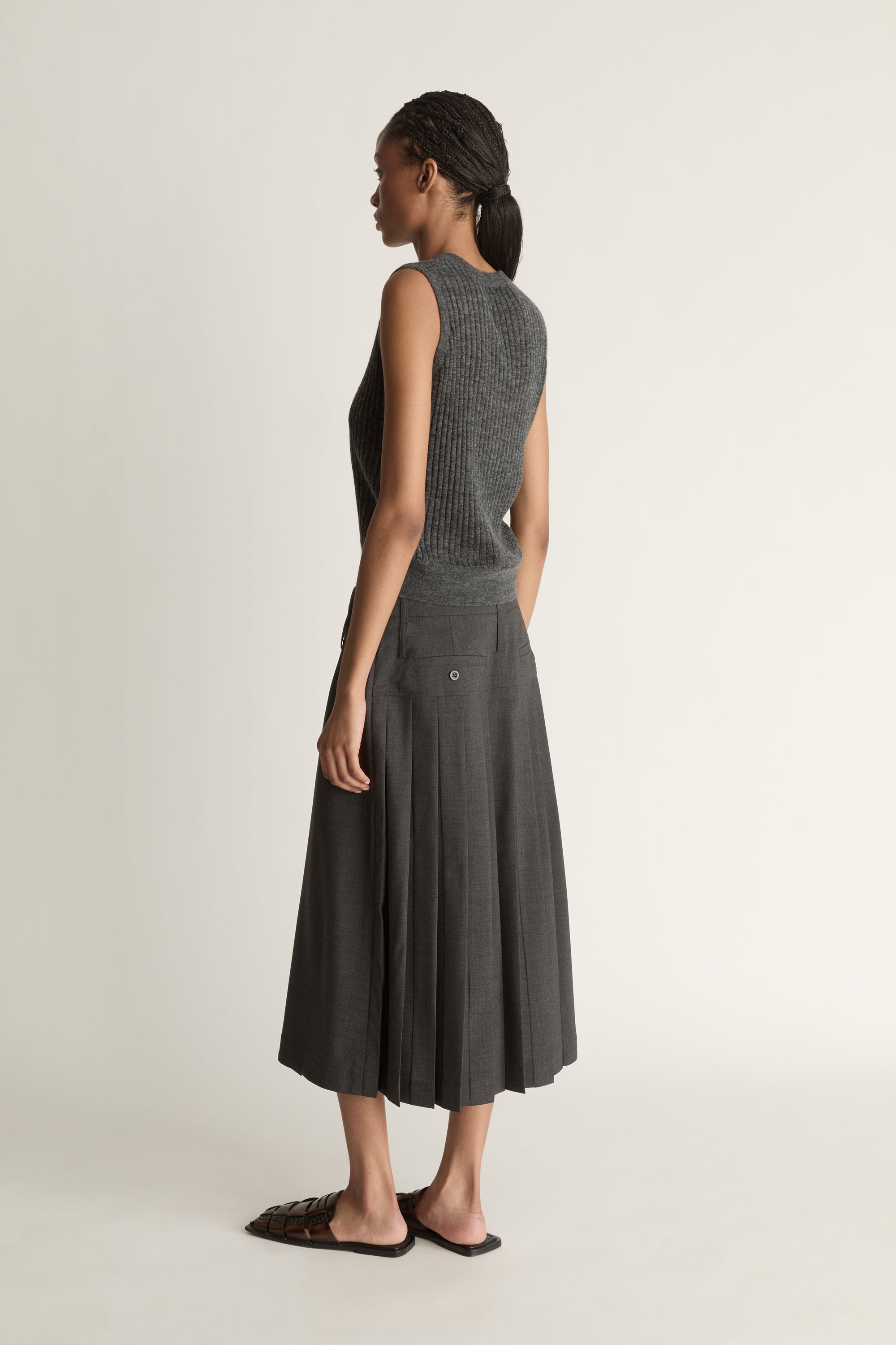 Woman wearing a dark gray sleeveless v neck knit top and skirt on a white background