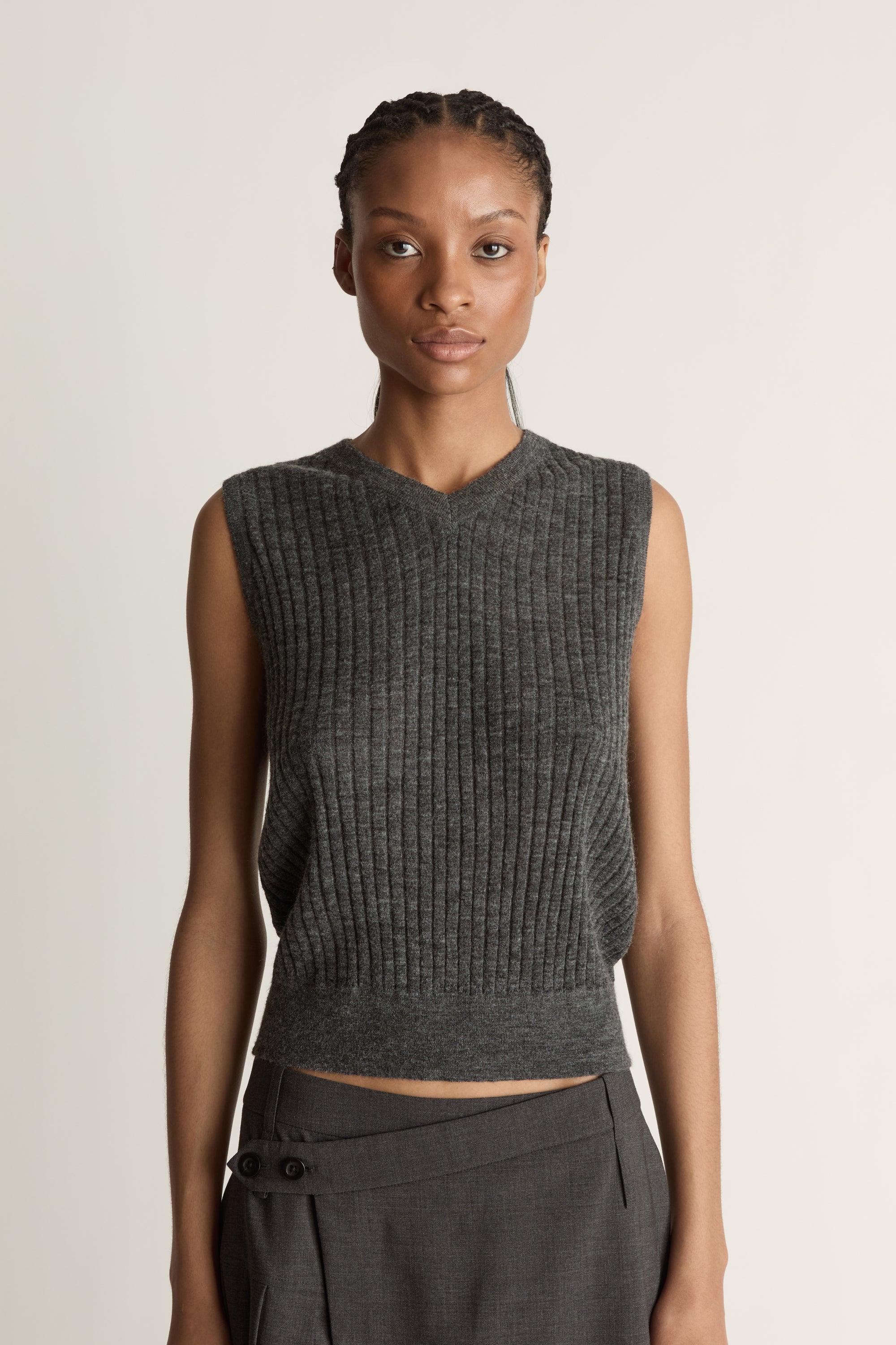 Woman wearing a dark gray sleeveless v neck knit top and skirt on a white background