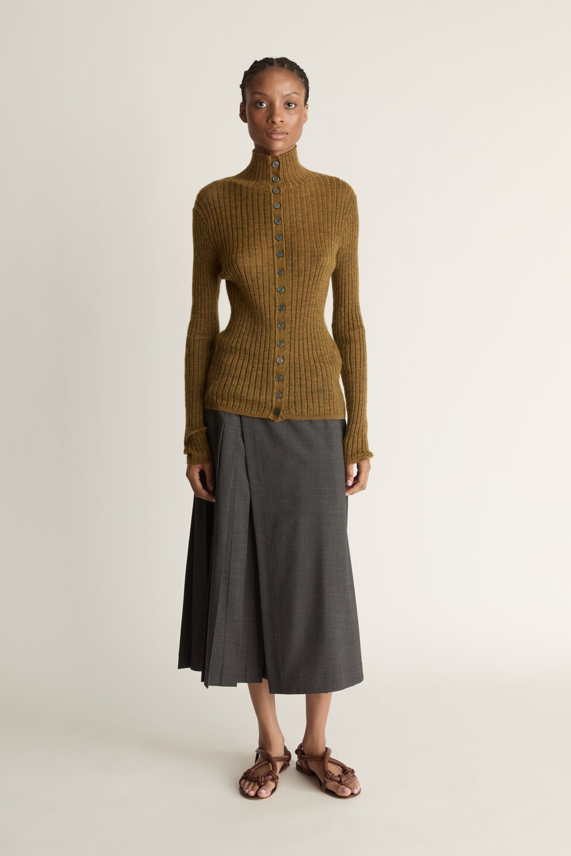 Woman wearing a brown ribbed sweater and gray skirt on a beige background