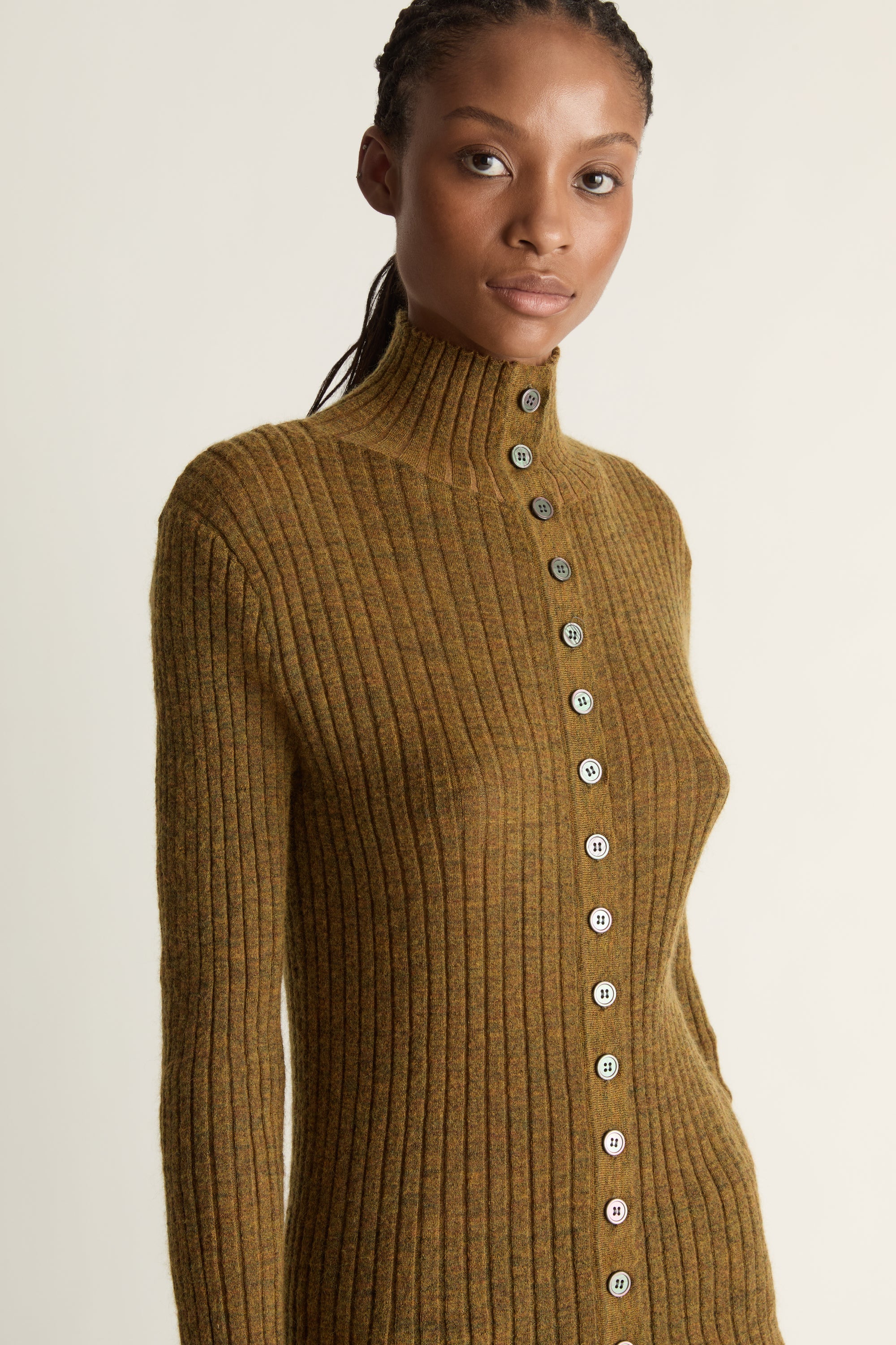 Woman wearing a brown ribbed sweater with button details on a plain background