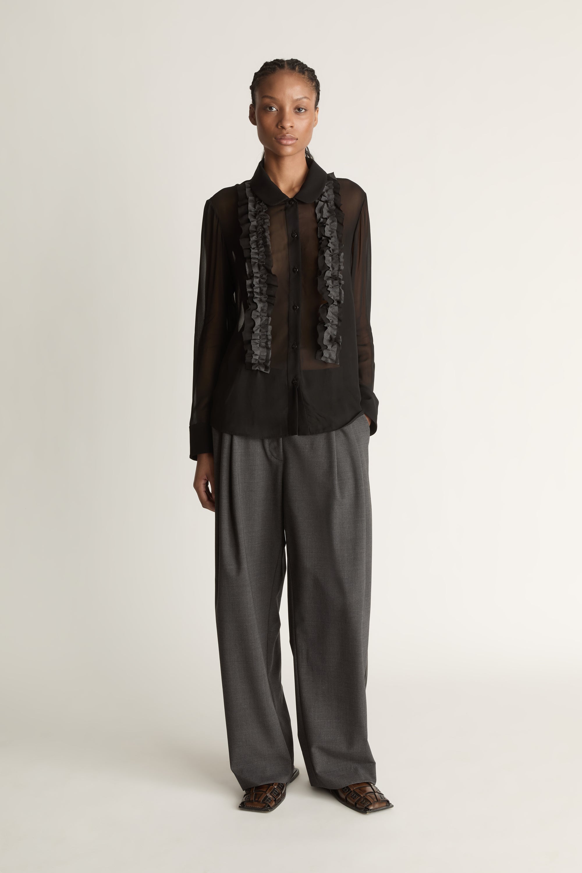 Woman wearing Black sheer shirt and grey trousers on a white background