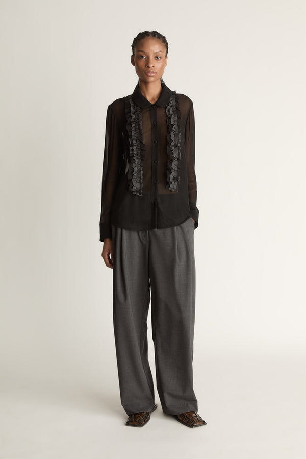 Woman wearing Black sheer shirt and grey trousers on a white background