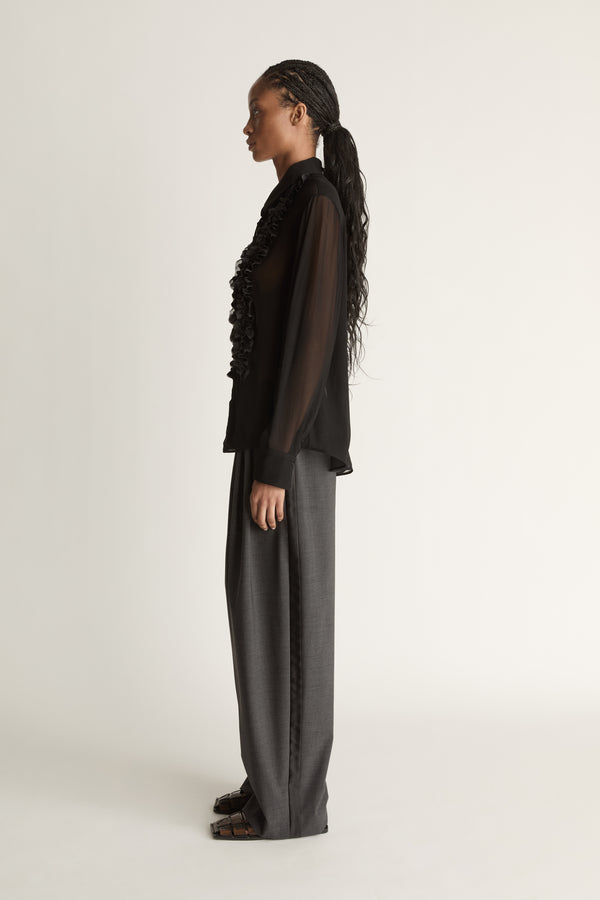 Woman wearing a black sheer shirt and grey trousers on a white background