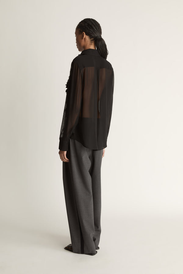 Woman wearing Black sheer shirt and grey trousers on a white background