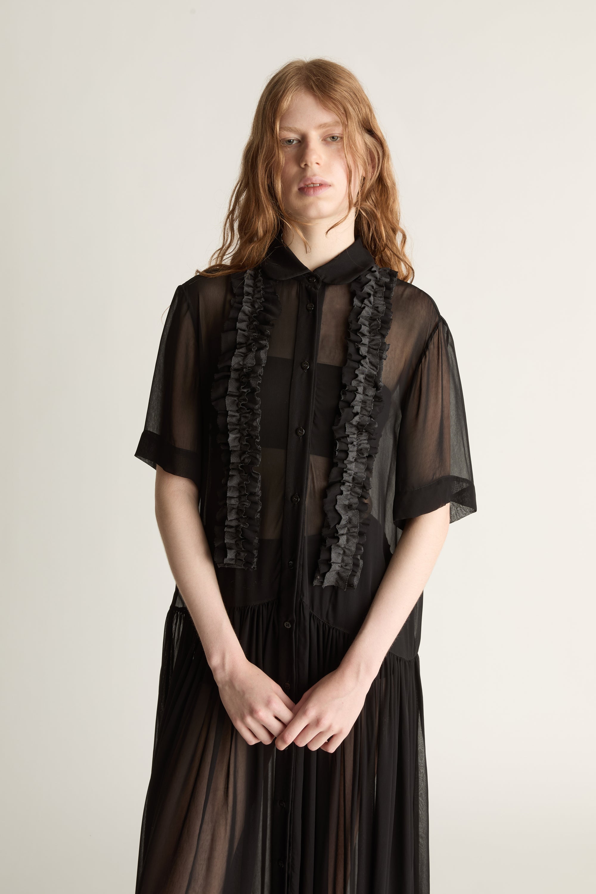 Woman wearing a black dress with sheer sleeves and lace details on a white background