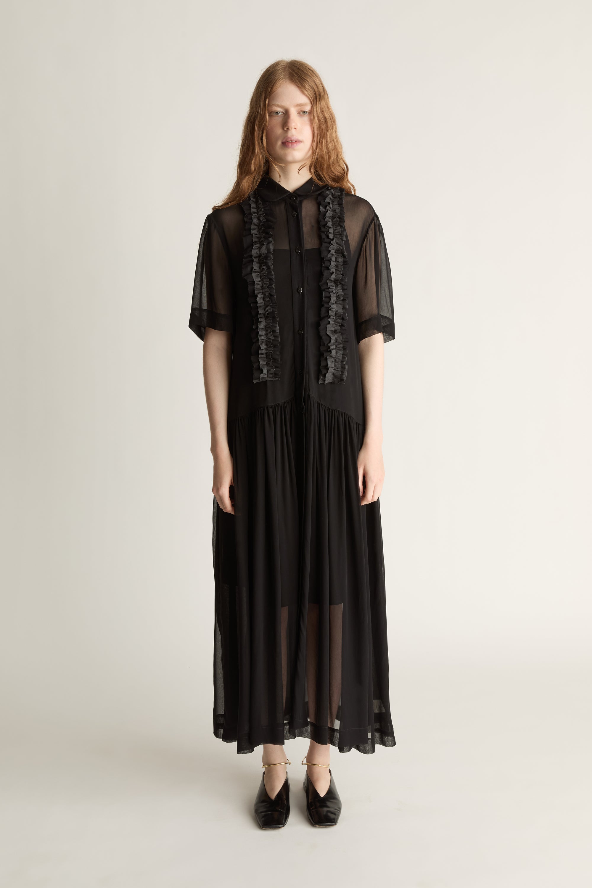Woman wearing a black dress with sheer sleeves and lace details on a white background