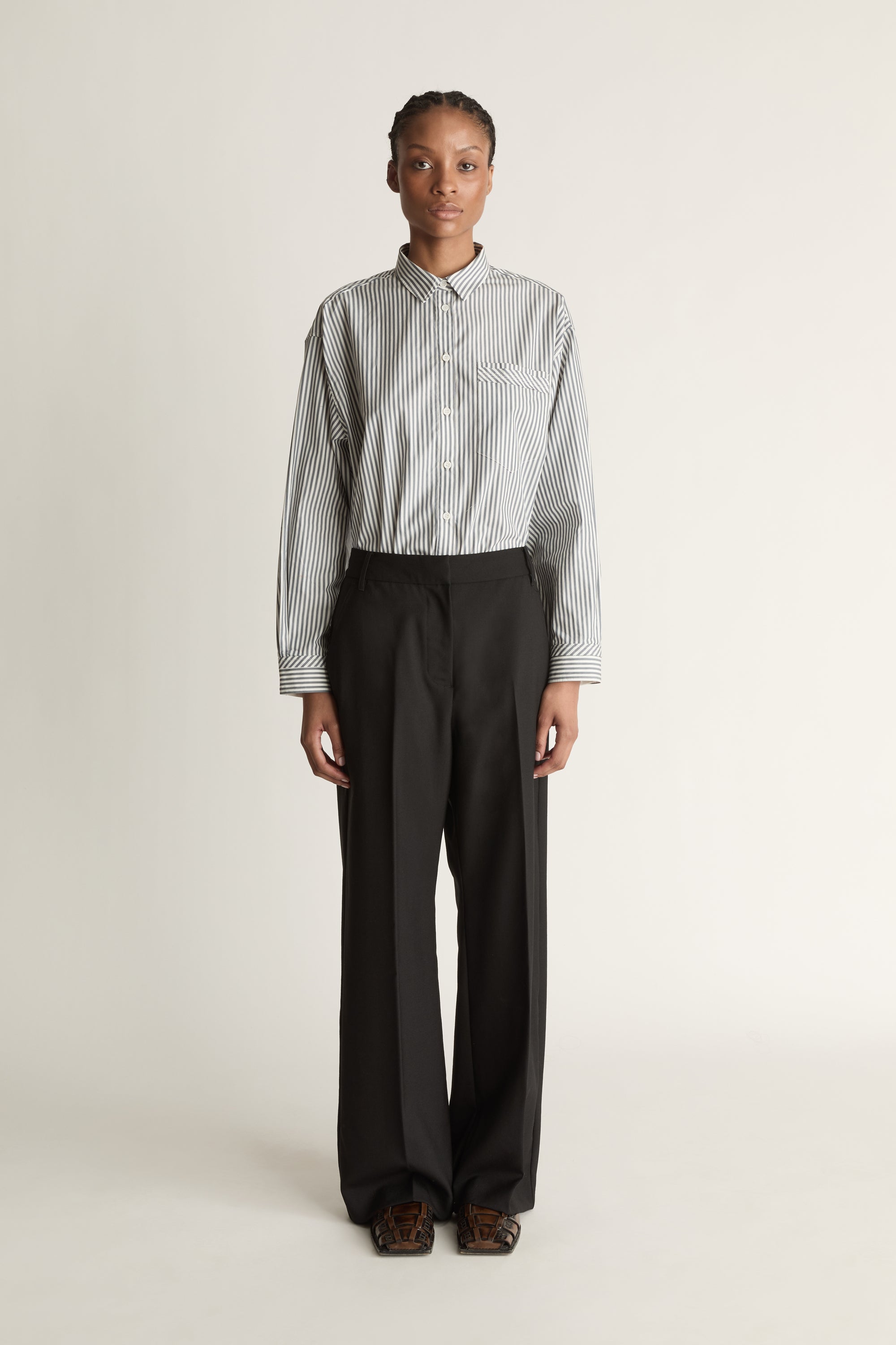 Person wearing a striped shirt and black pants on a white background