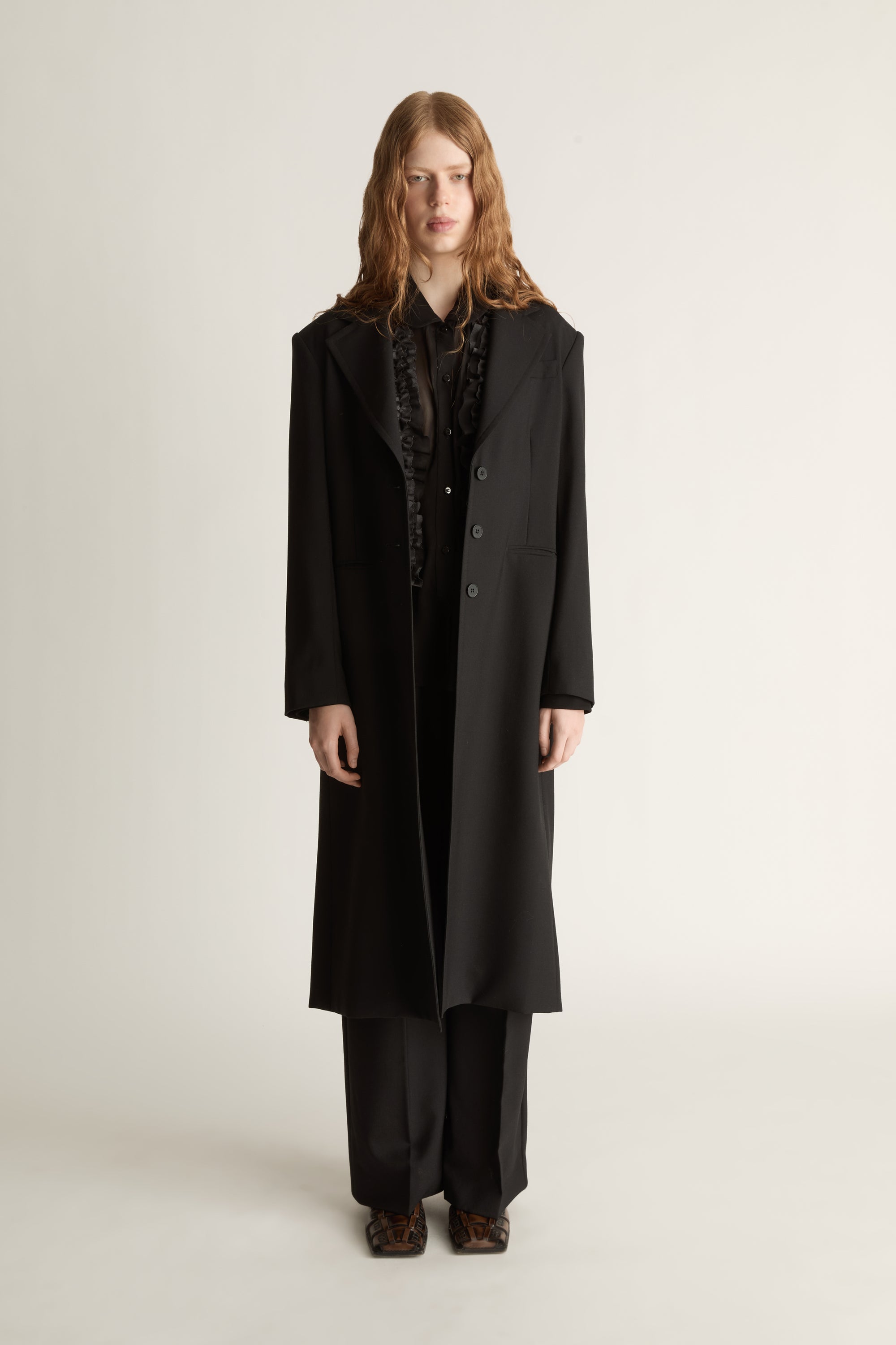 Person wearing a long black coat on a plain background