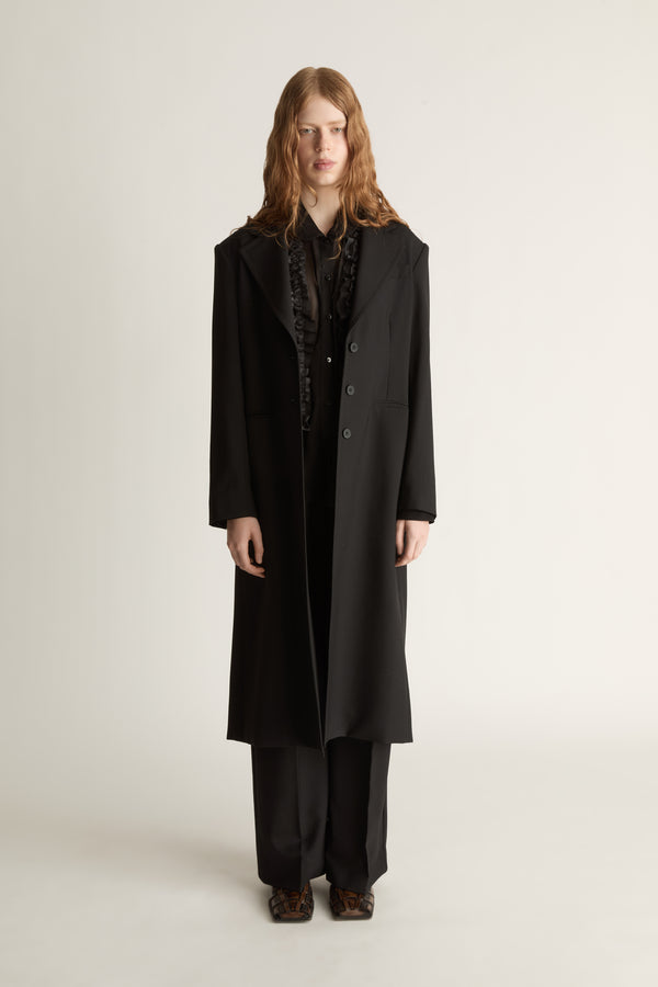 Person wearing a long black coat on a plain background