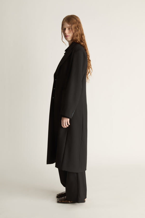 Person wearing a long black coat on a plain background