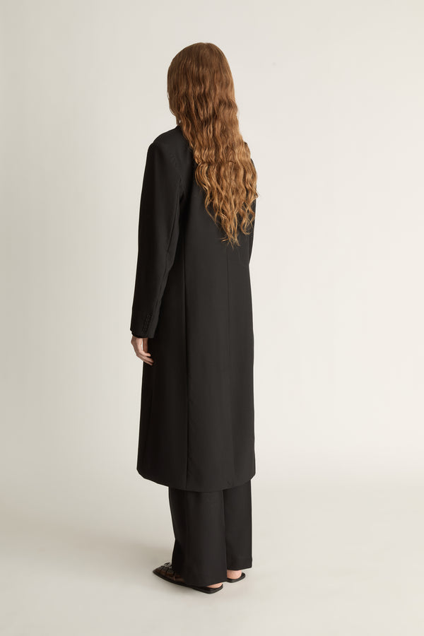 Person wearing a long black coat on a plain background