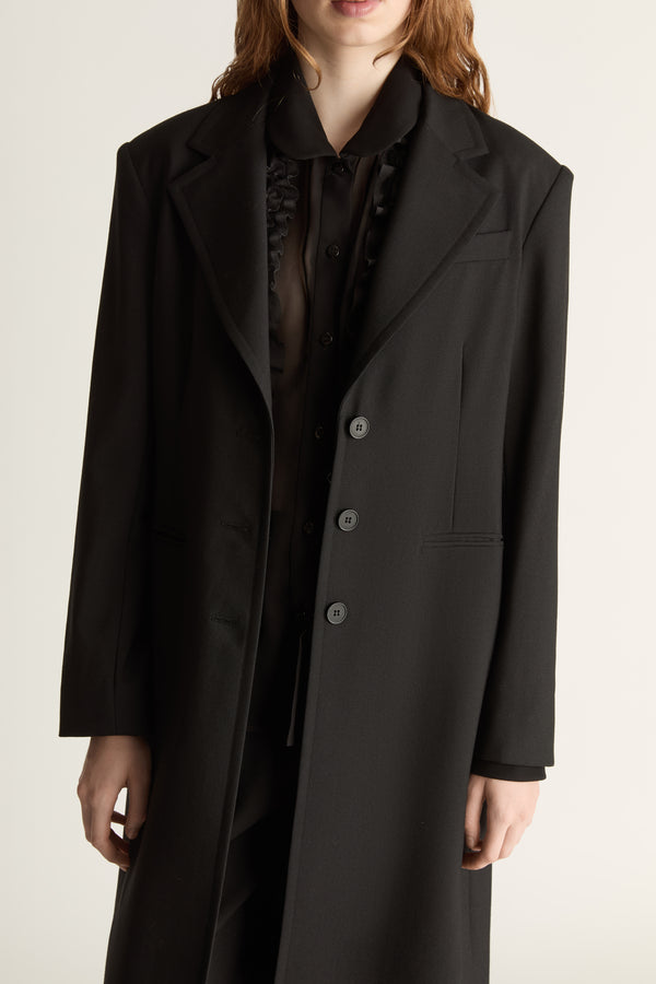 Person wearing a long black coat on a plain background
