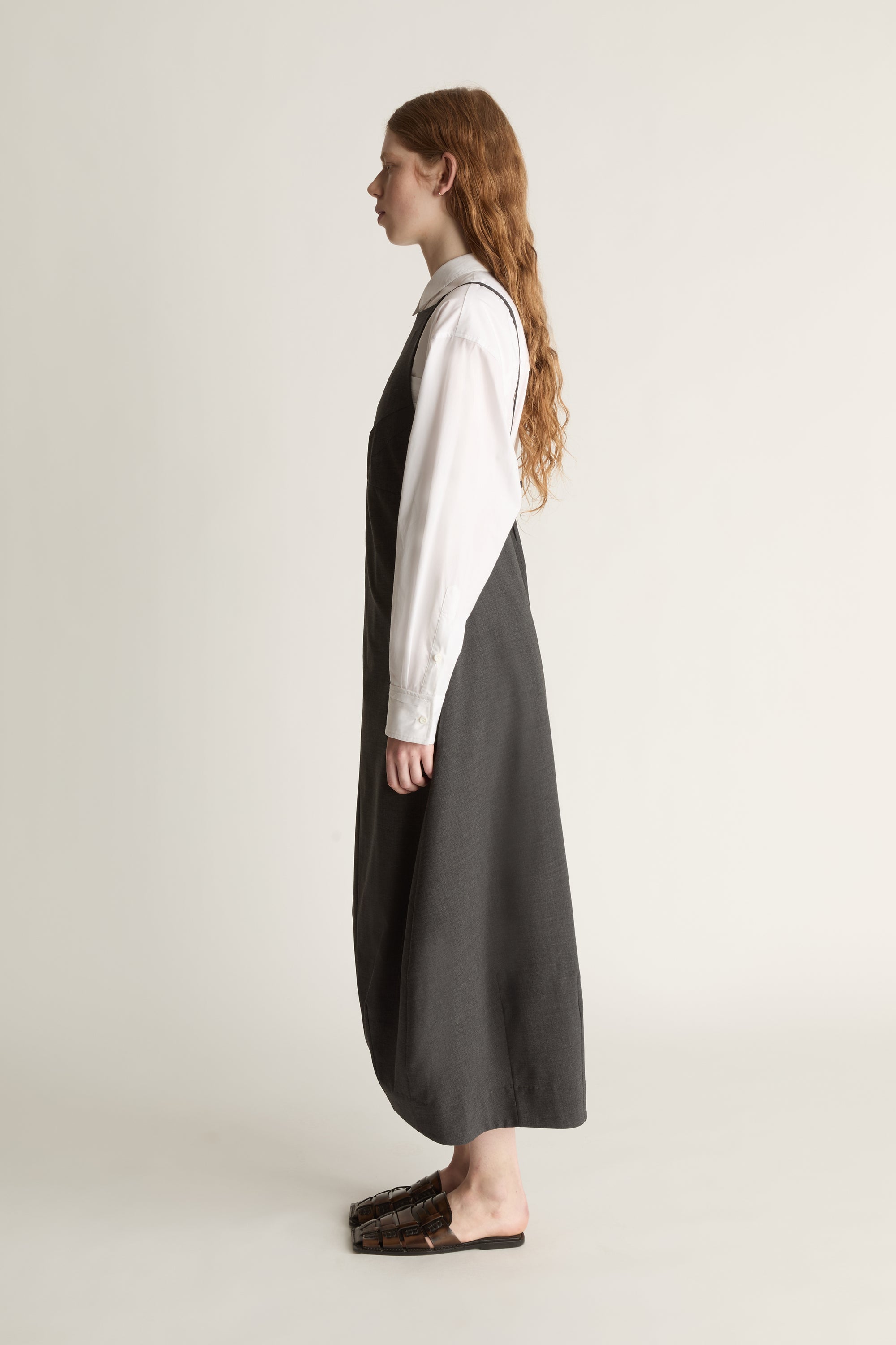 Person wearing a long dark apron style dress over a light shirt on a plain background