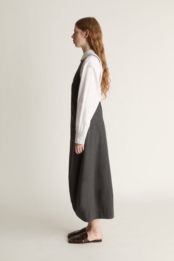 Person wearing a long dark apron style dress over a light shirt on a plain background
