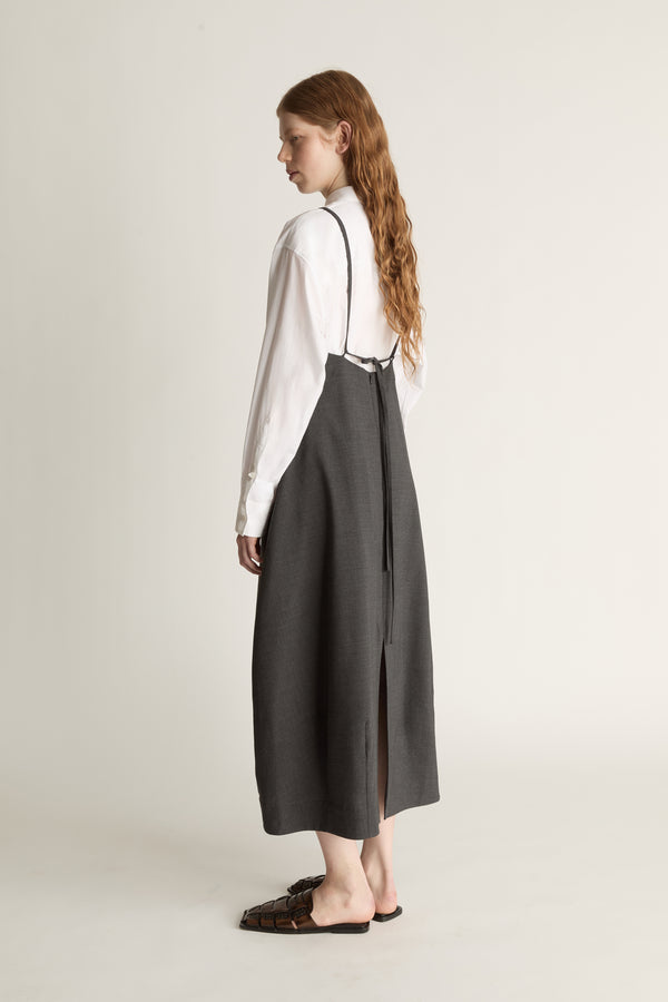 Person wearing a long dark apron style dress over a light shirt on a plain background