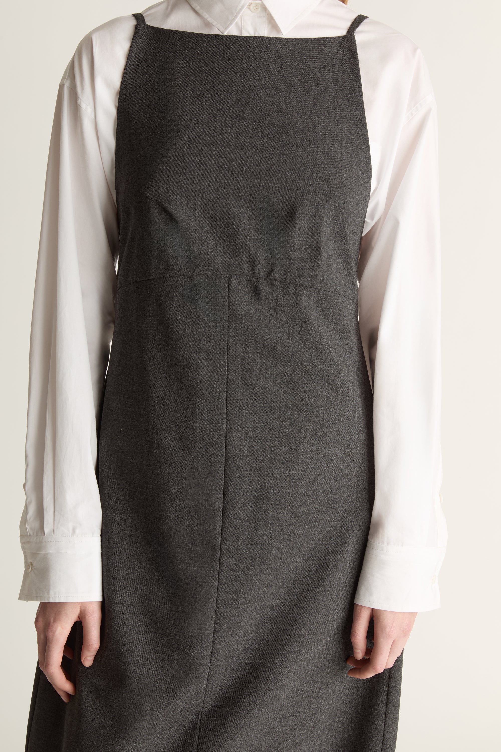 Person wearing a long dark apron style dress over a light shirt on a plain background