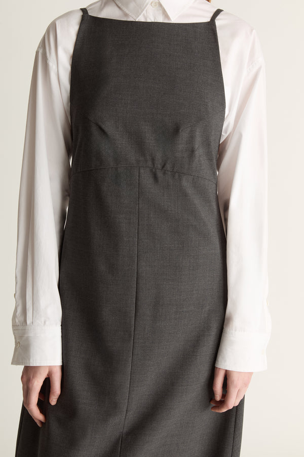 Person wearing a long dark apron style dress over a light shirt on a plain background