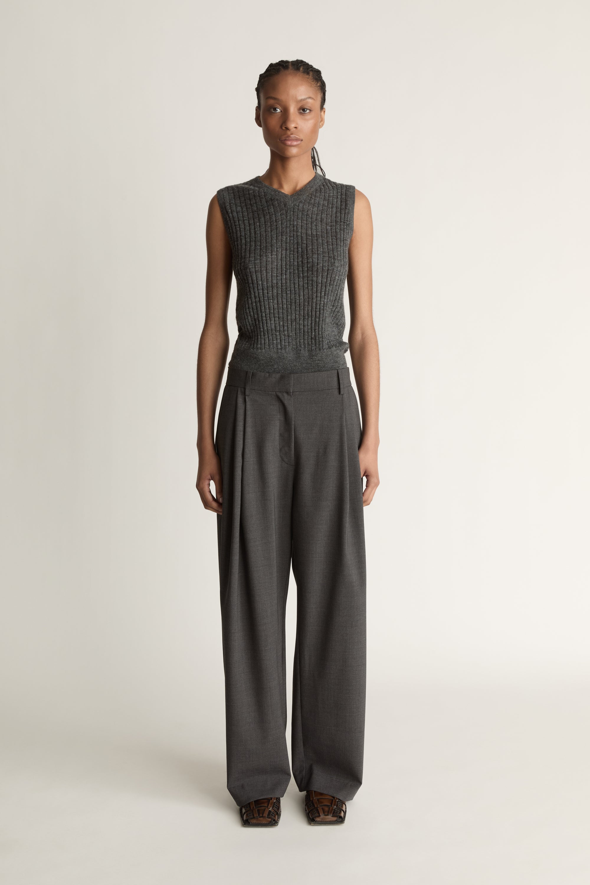 Woman wearing a sleeveless knitted top and wide-leg pants on a plain background