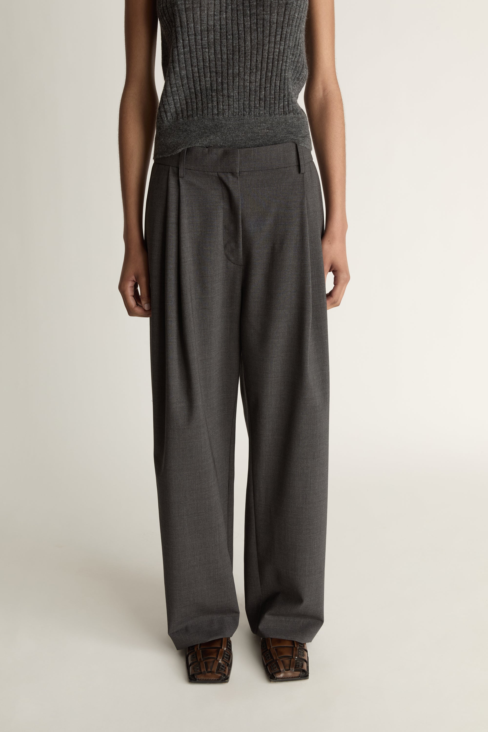 Woman wearing a sleeveless knitted top and wide-leg pants on a plain background