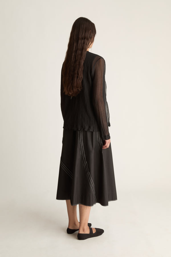 Back view of a woman with long wavy hair in a sheer black cardigan and black midi skirt