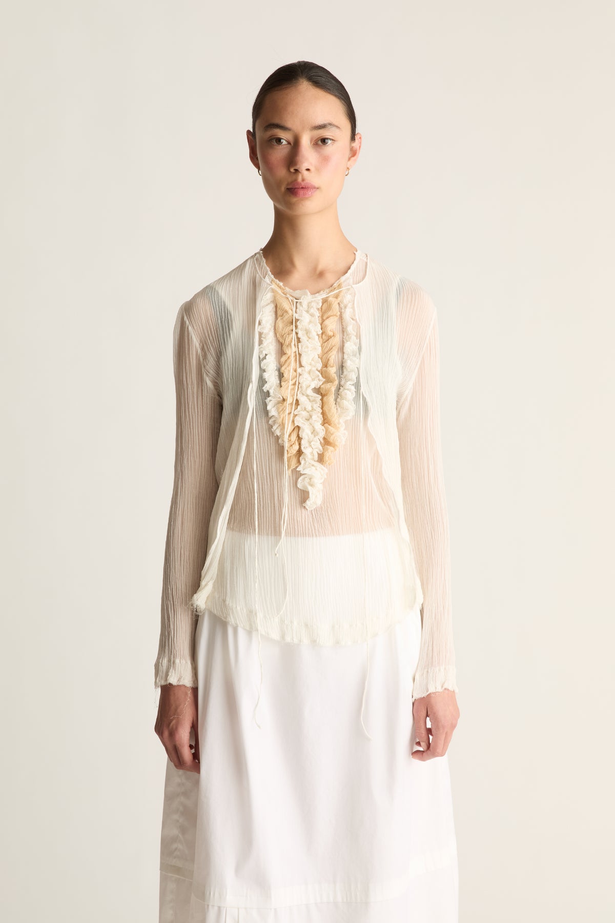 Close-up of a sheer cream cardigan layered over a ruffle front top with a scalloped hem