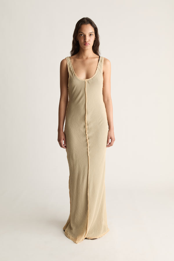 Front view of a woman wearing a beige sleeveless scoop-neck maxi dress against a white studio background