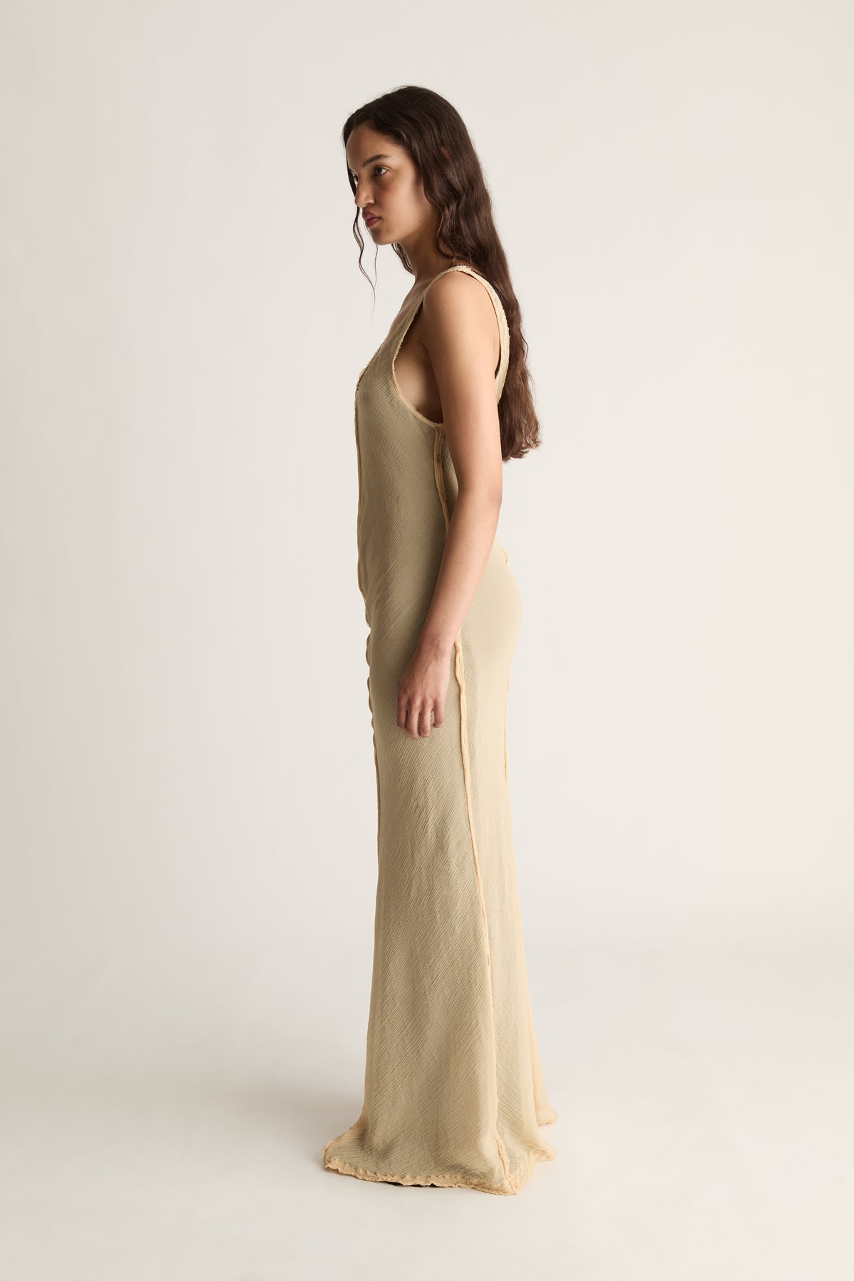 Side profile of a woman in a fitted beige sleeveless maxi dress with scoop neckline