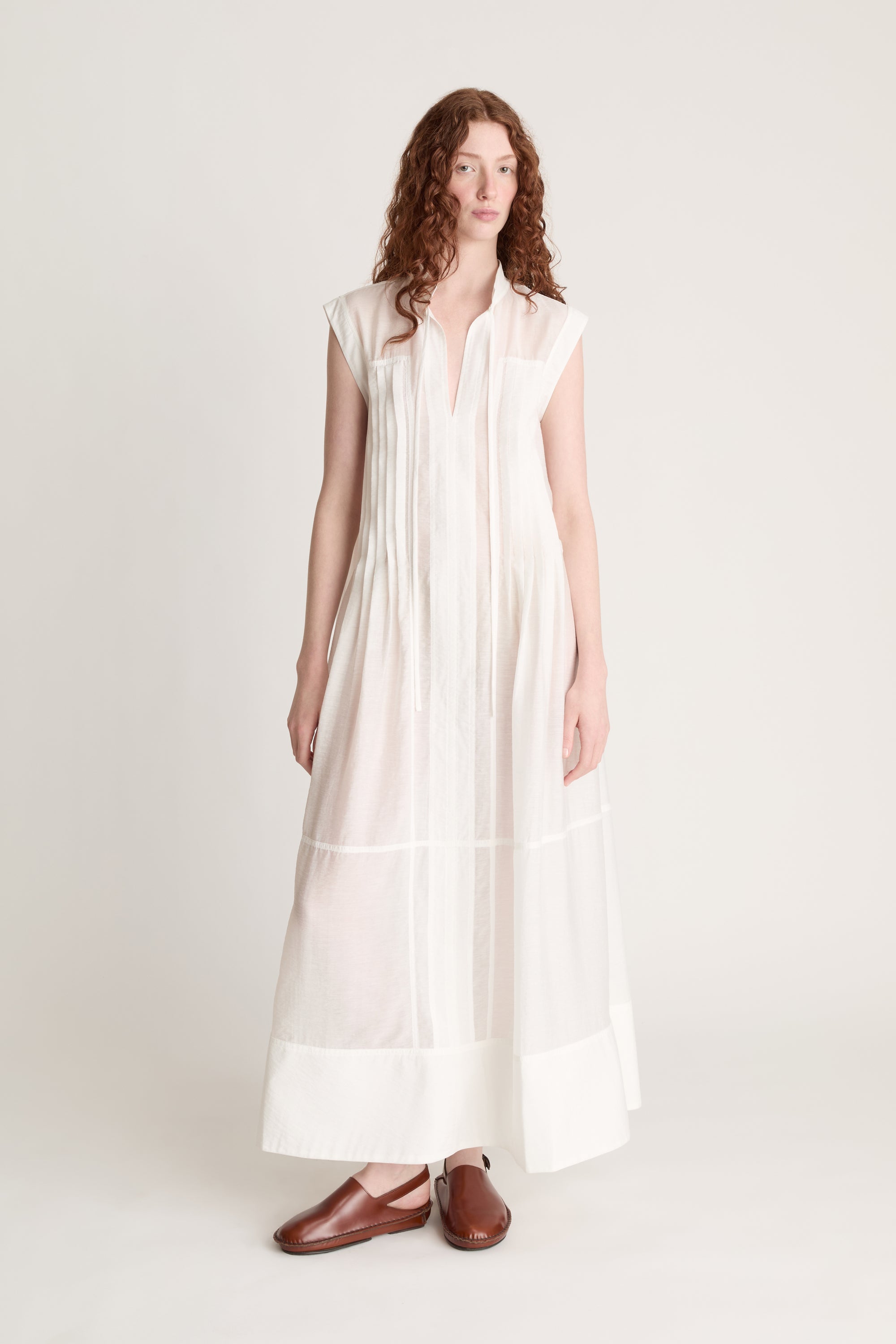 Woman wearing a long white dress with brown shoes on a white background