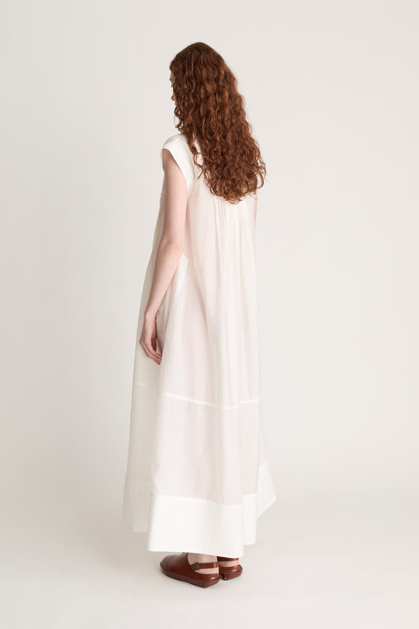 Woman wearing a long white dress with brown shoes on a white background