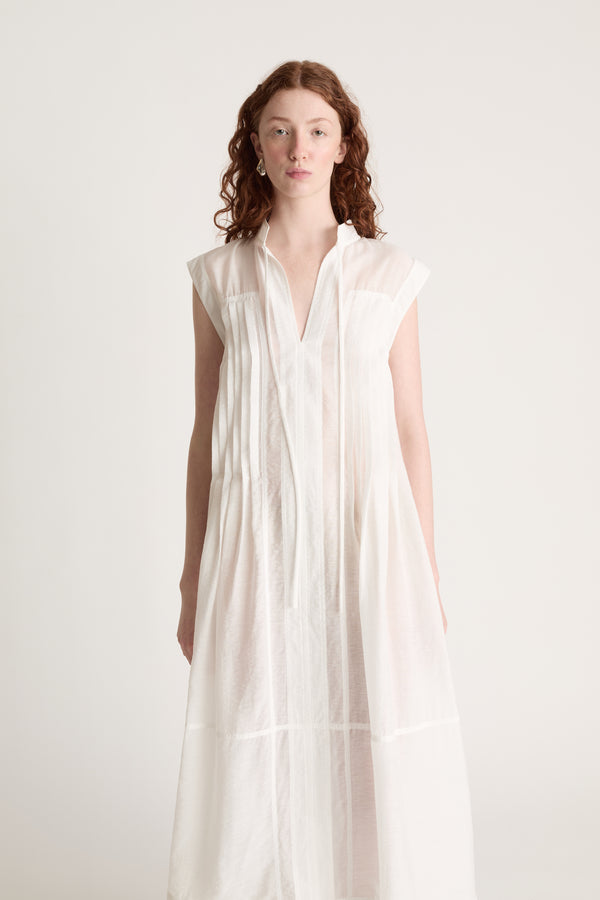 Woman wearing a long white dress with brown shoes on a white background