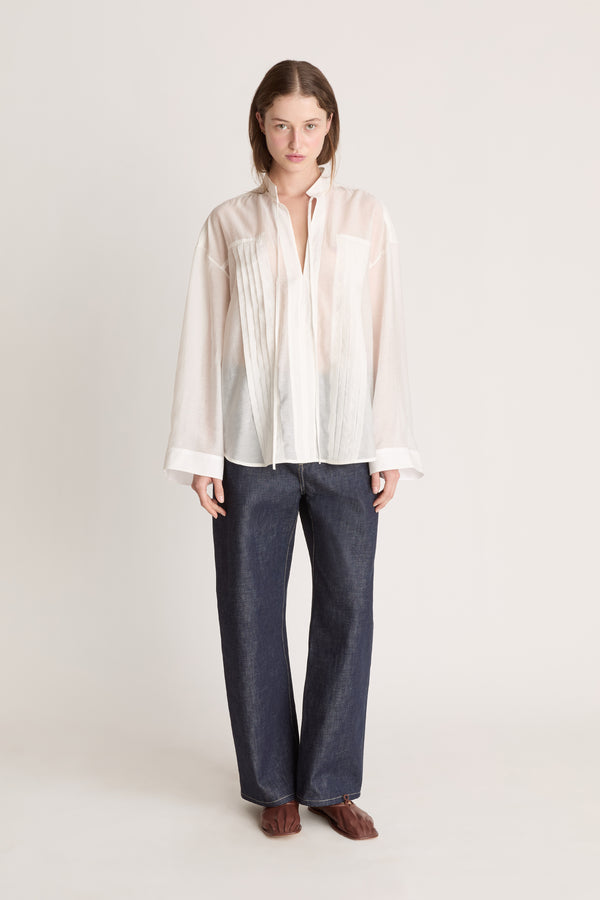 Person wearing a light-colored blouse and dark pants on a white background