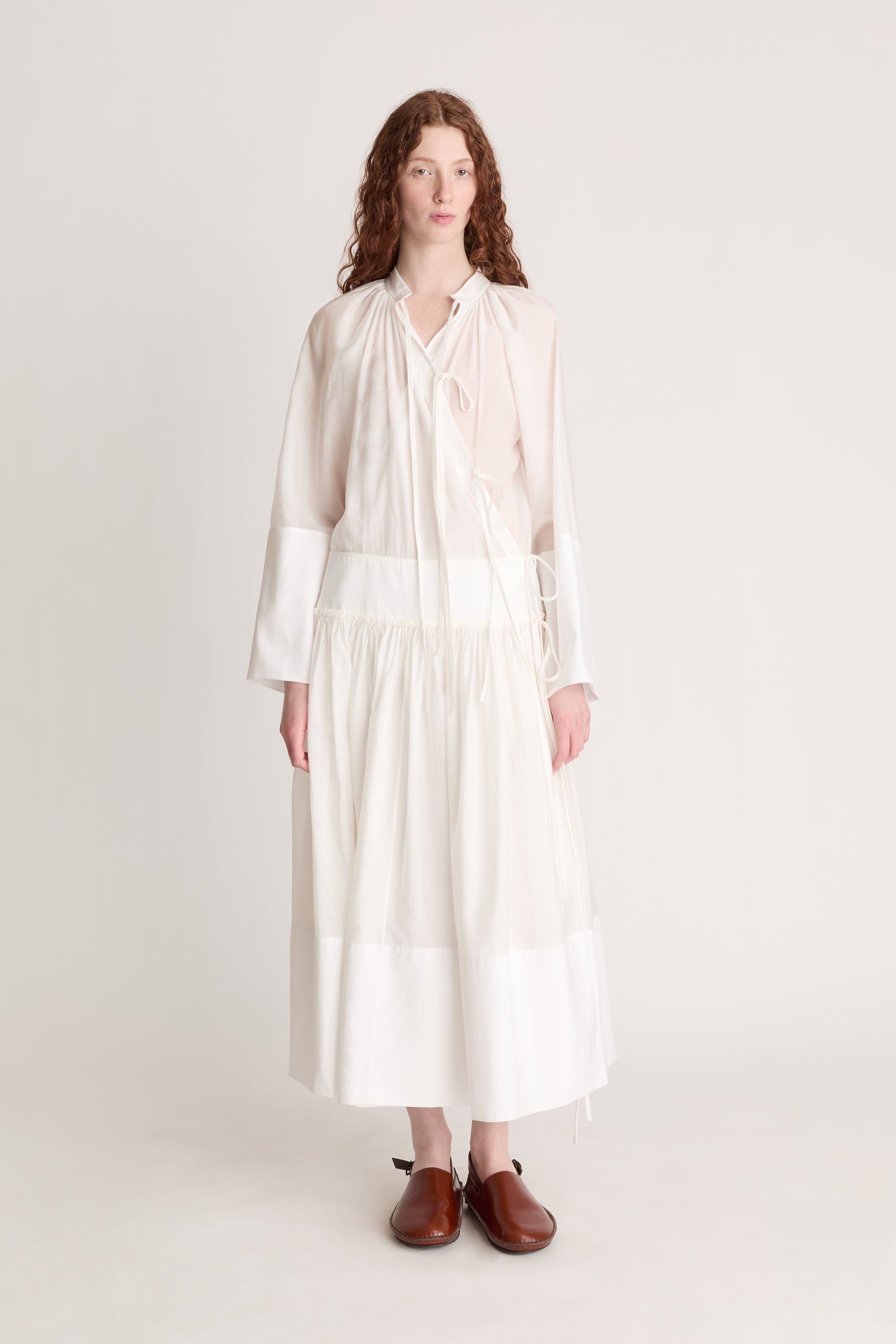 A woman wearing a long white dress with a tie detail, on a plain background