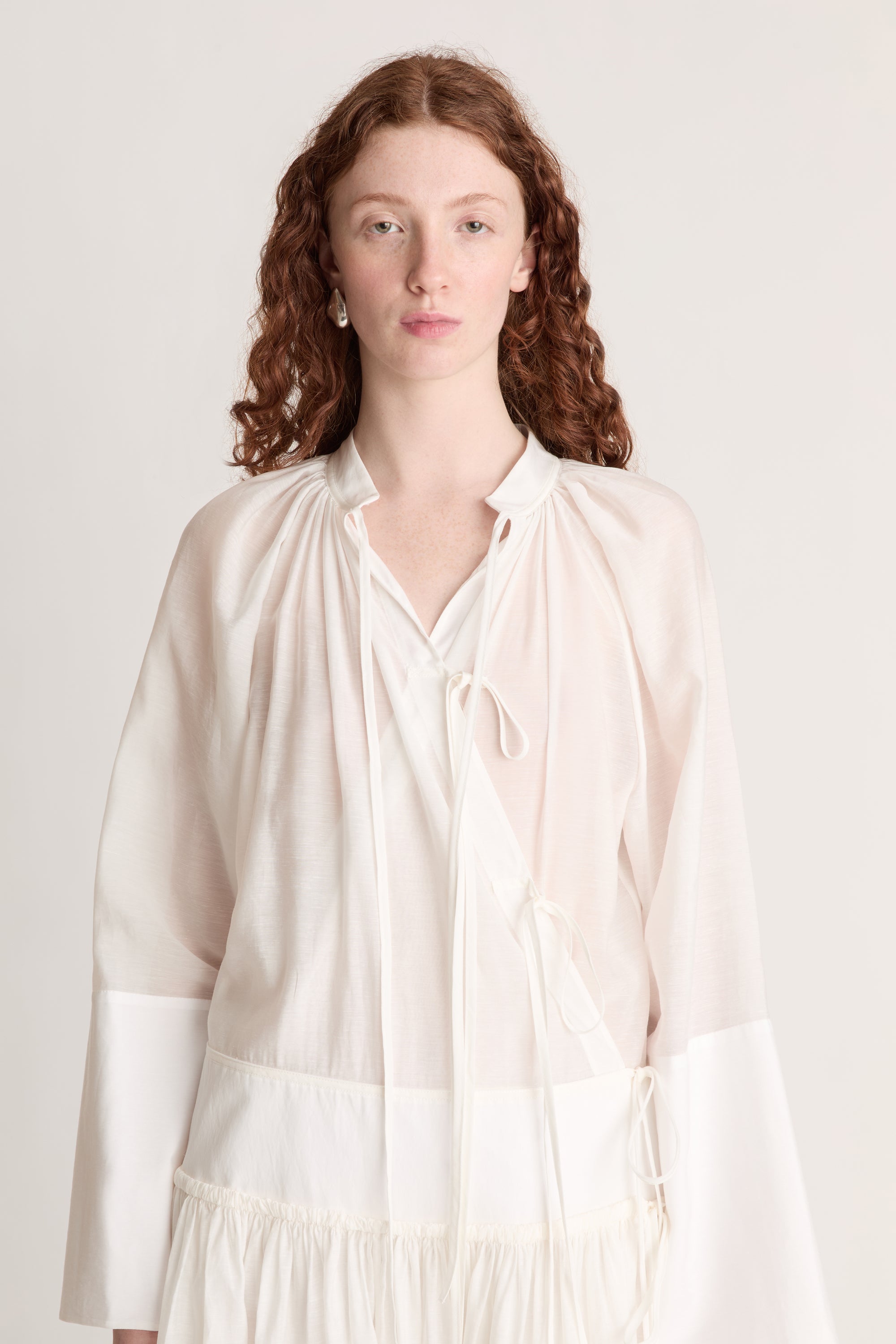 A woman wearing a long white dress with a tie detail, on a plain background