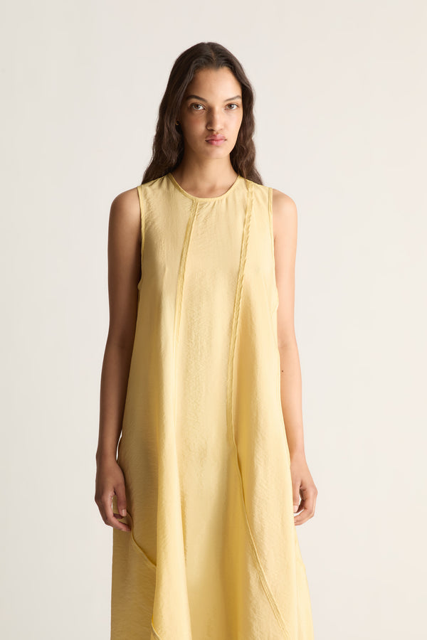 Close-up of a woman in a pale yellow sleeveless A-line dress with curved panel seams and round neckline